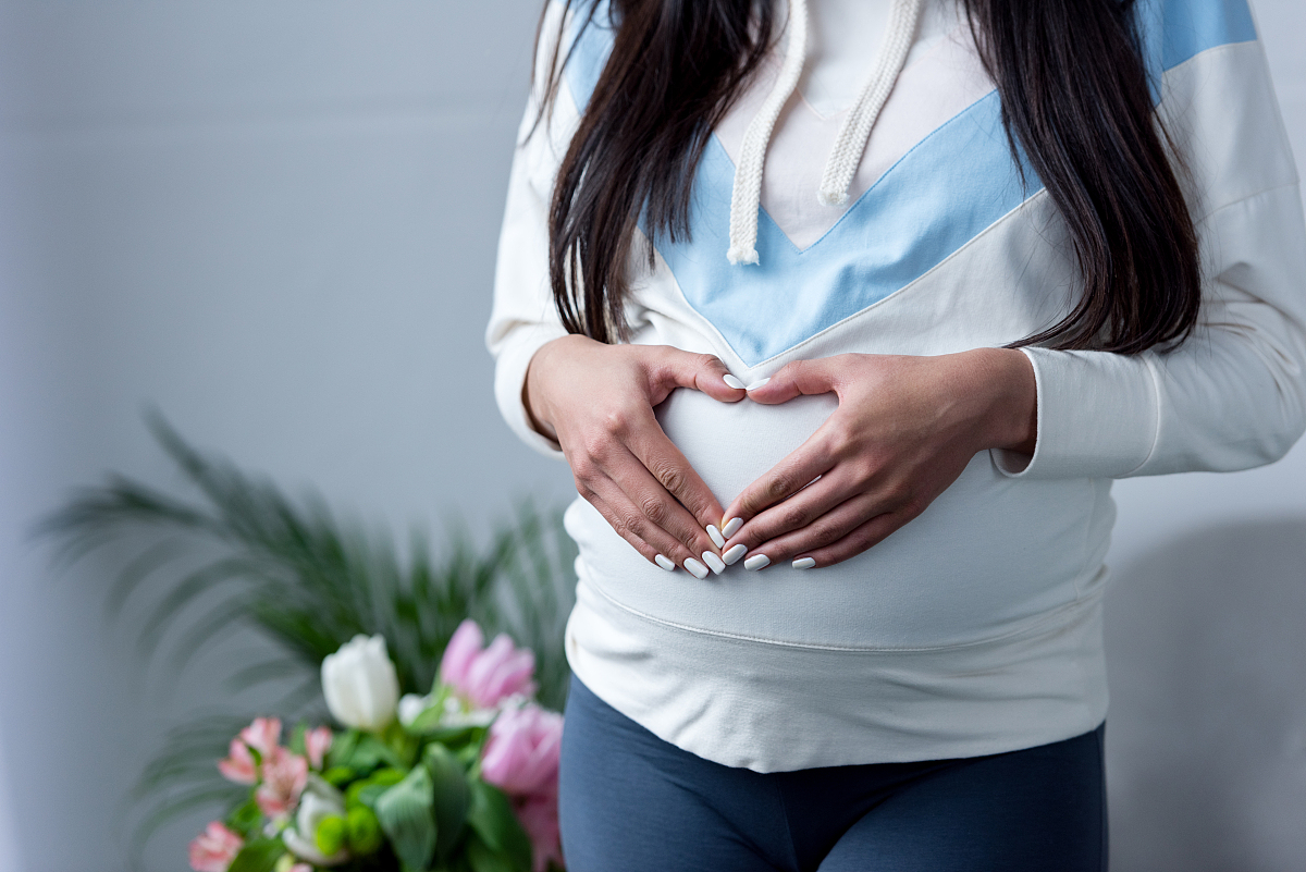 cropped view of pregnant girl making heart symbol with hands on 