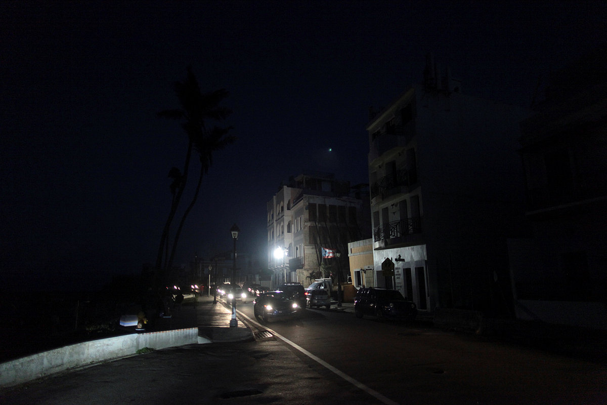 cars drive on a street in the light of a generator-powered lamp 