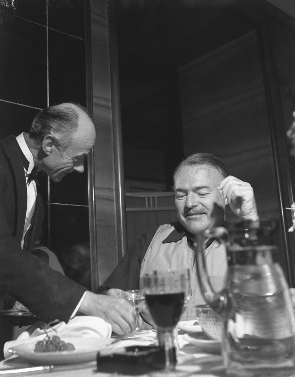 american writer ernest hemingway, sitting at a restaurant table,
