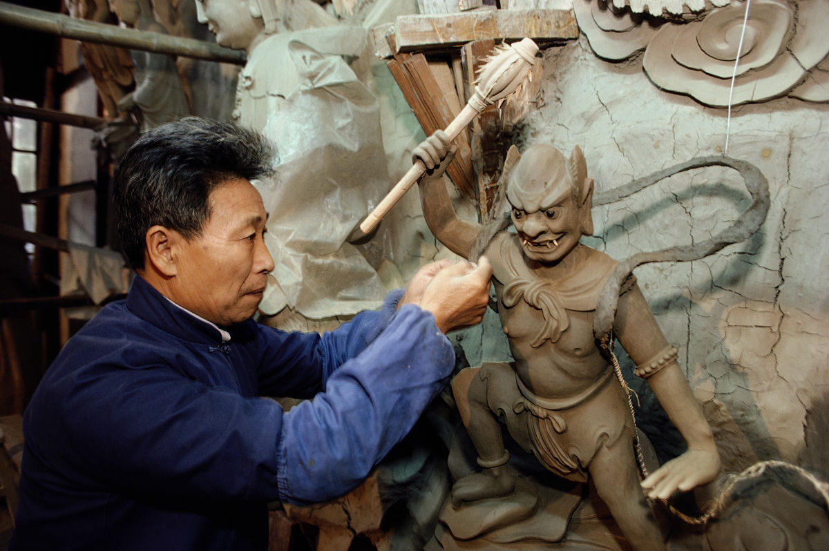 中国,工坊内雕刻塑像的工人.mature man carving statue in workshop 