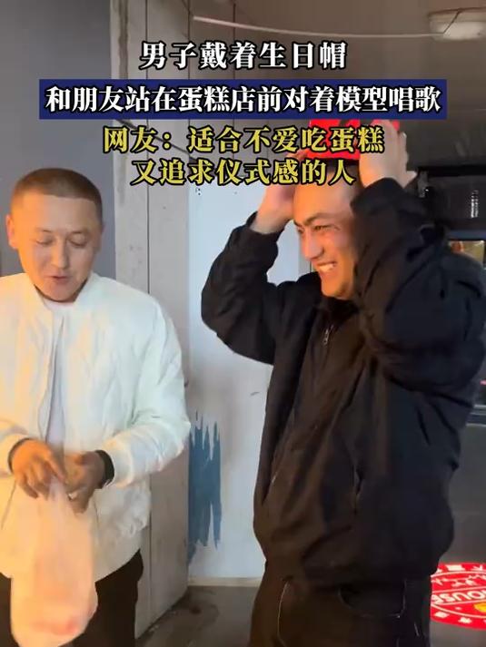 男子戴着生日帽,和朋友站在蛋糕店前对着模型唱歌