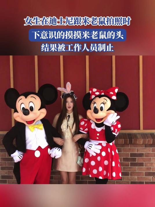 女生跟米老鼠拍照时,下意识的摸摸米老鼠头,结果被工作人员制止