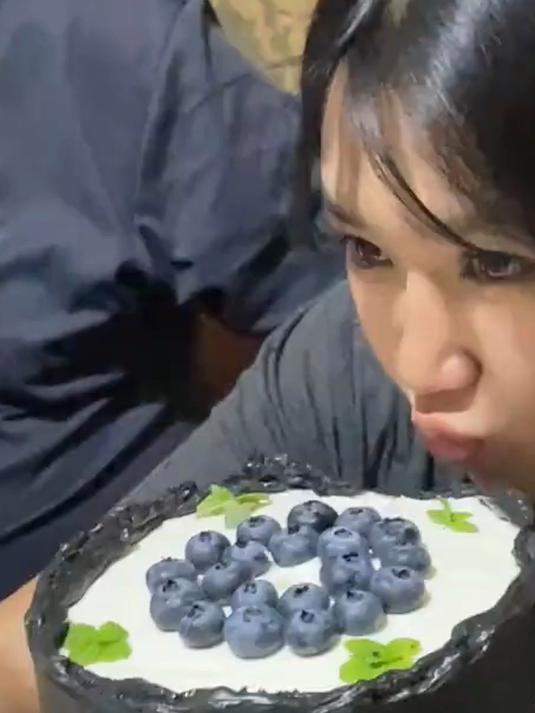 女儿拿着手机要和蛋糕合影,一旁的爸爸把女儿头拍进蛋糕里