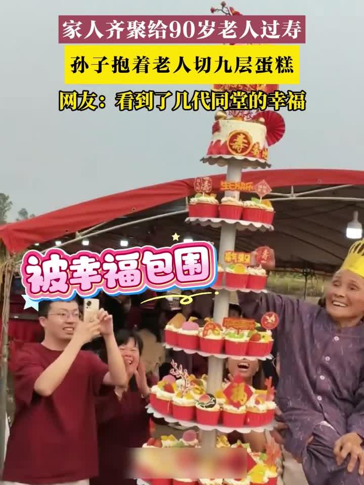 家人齐聚给90岁老人过寿，孙子抱着老人切九层蛋糕