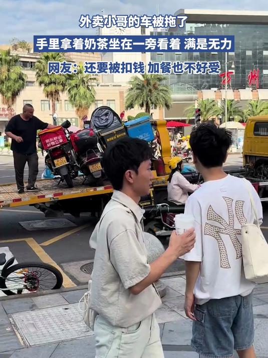 外卖小哥的车被拖了，手里拿着奶茶坐在一旁看着 满是无力