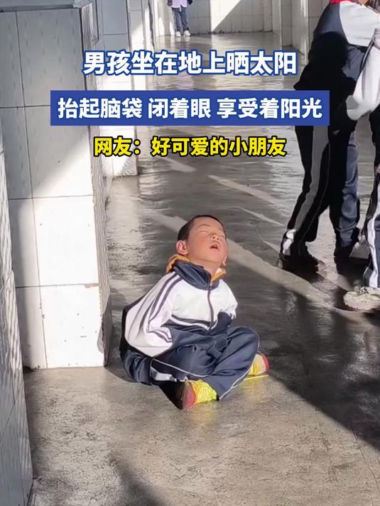 男孩坐在地上晒太阳,抬起脑袋,闭着眼,享受着阳光