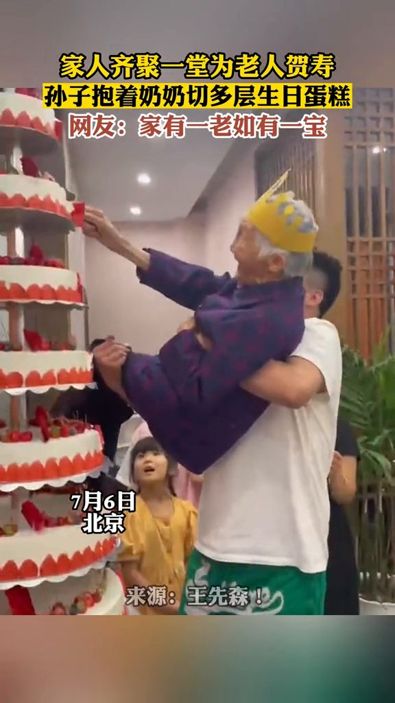家人齐聚一堂为老人贺寿,孙子抱着奶奶切多层生日蛋糕