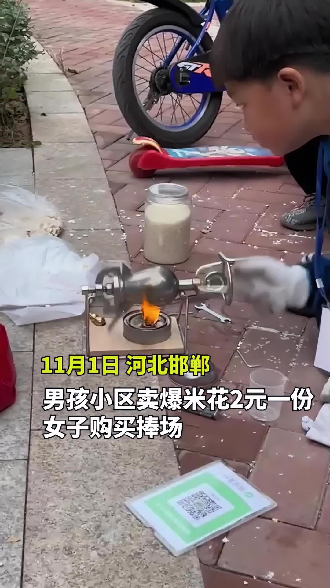 男孩在小区用迷你爆米花机摆摊,女子2元购买捧场“照顾生意”