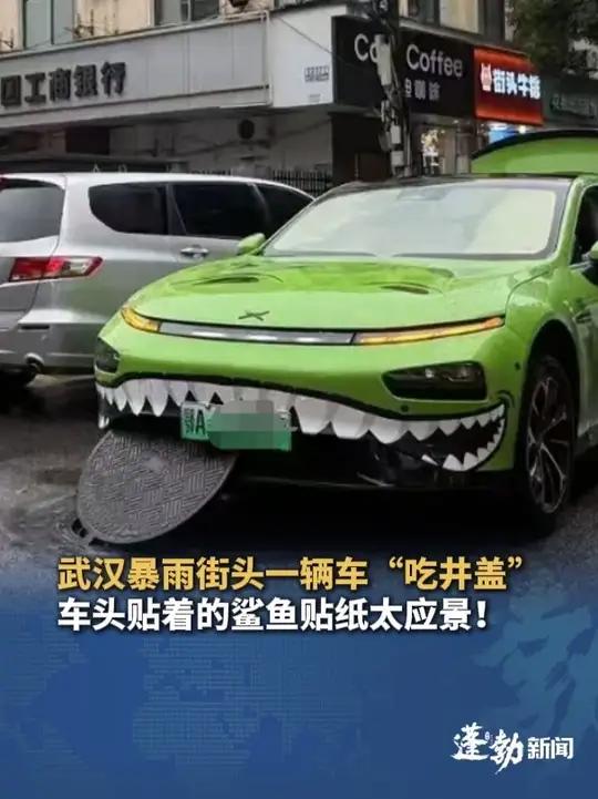 武汉暴雨街头一辆车“吃井盖”,车头贴着的鲨鱼贴纸太应景,网友:好家伙!这牙不是白长的
