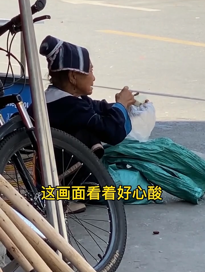 中午了奶奶东西还没卖完,一个人蹲在路边吃馒头