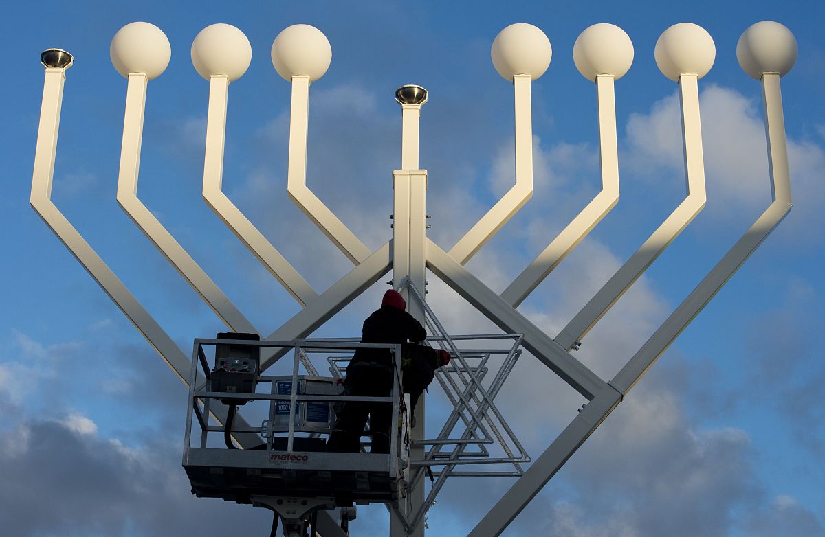 workers fasten a star of david on a giant menorah in front of th
