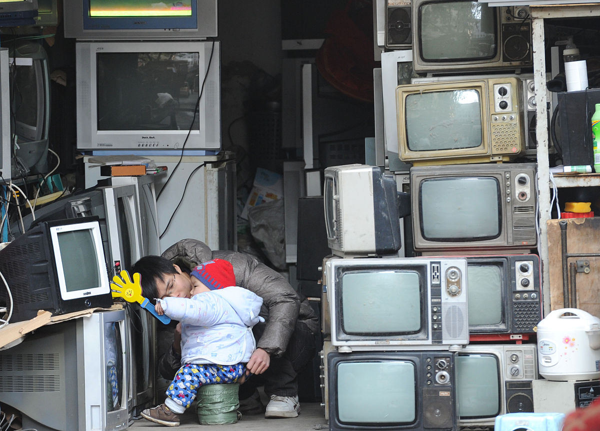 2011年12月15日,南京一名从事二手家电生意的商贩在报废电视机旁陪着