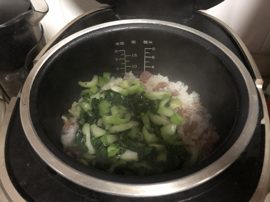 米饭煮至水快收干时,把炒过的青菜也倒入电饭煲中一起煮至结束