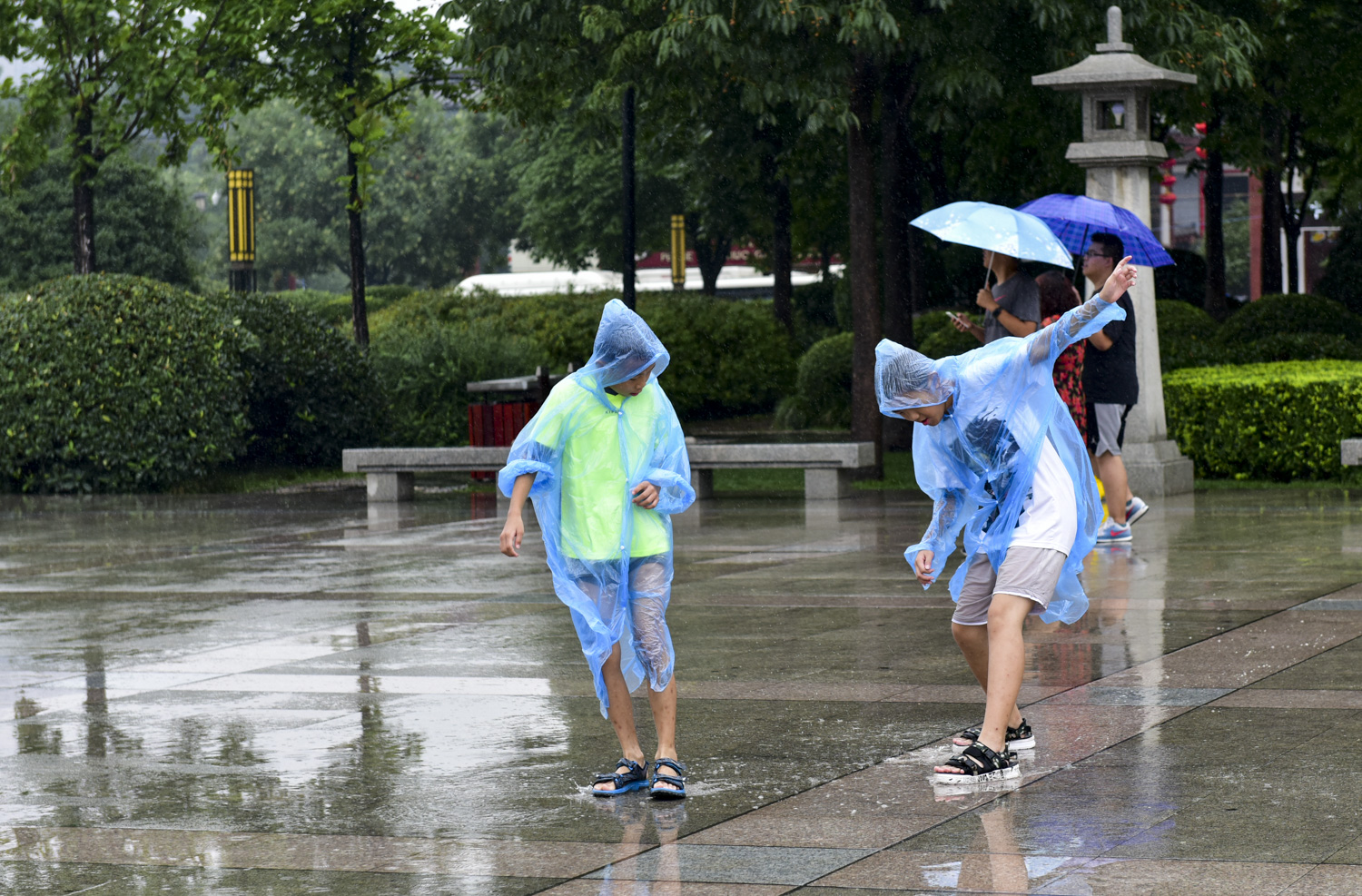 在雨中,两名穿雨衣的孩子玩水玩的不亦乐乎.