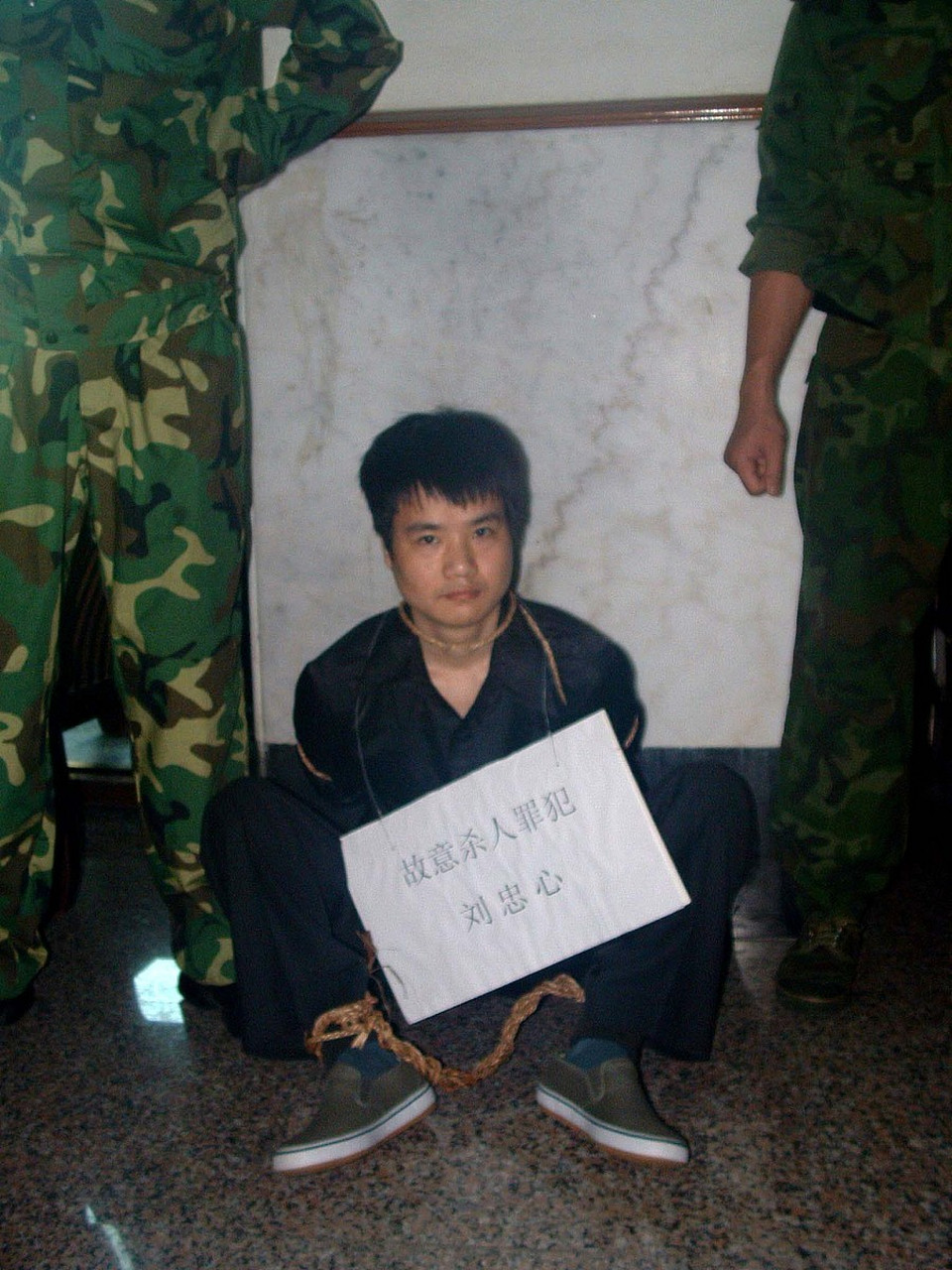 2005年,三亚,戴着脚镣的余伟 ,坐在地上,手拿电话,给家里人打着电话.