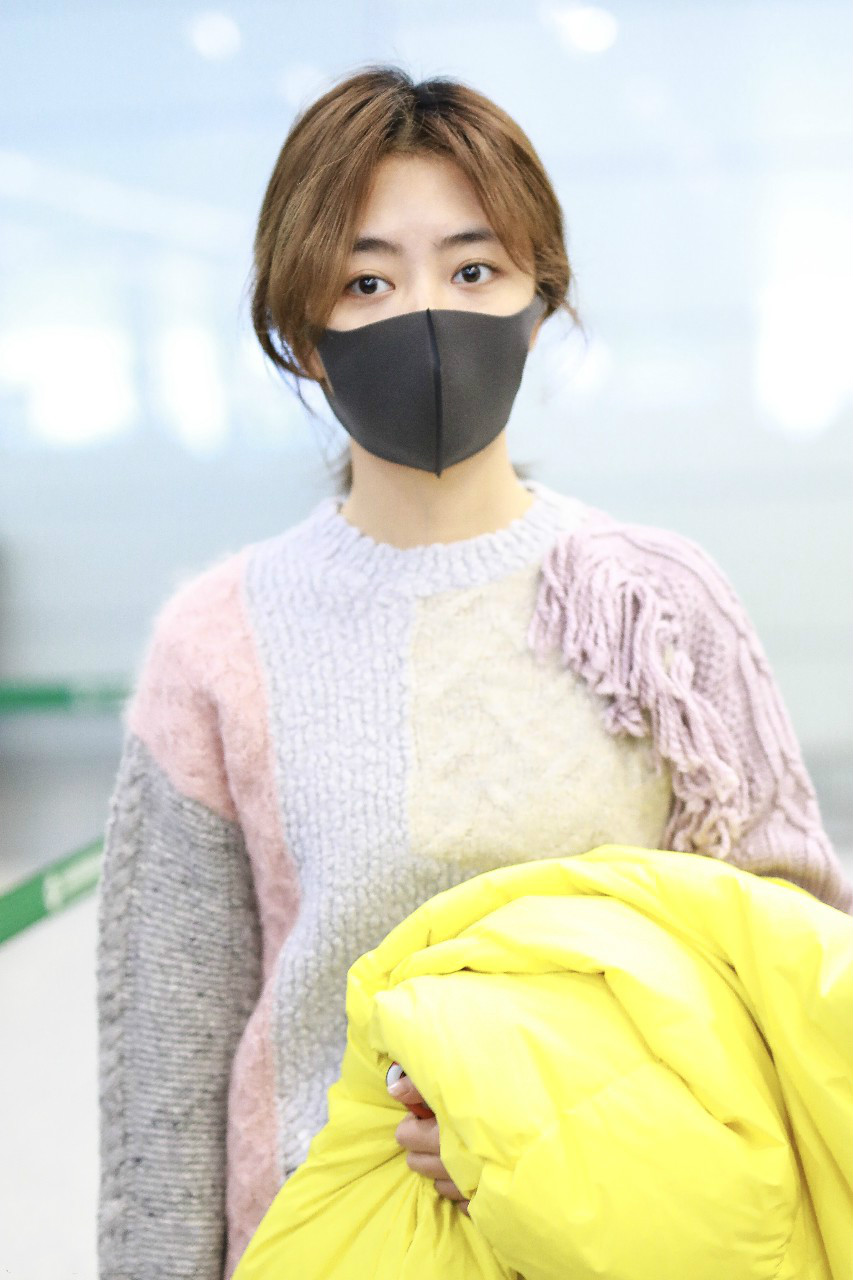 谭松韵戴口罩穿毛衣搭配牛仔裤现身机场,手里拿着黄色羽绒服