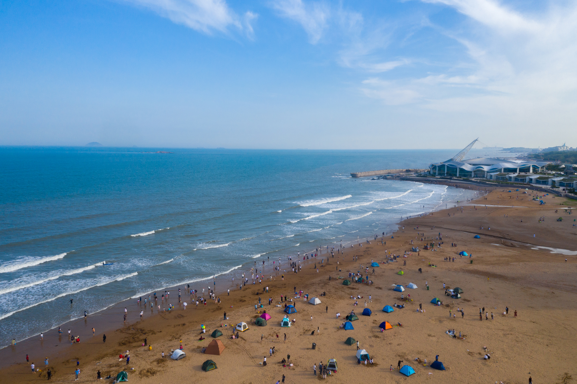 航拍青岛石老人海水浴场,天蓝蓝海蓝蓝,游客人头攒动流连忘返