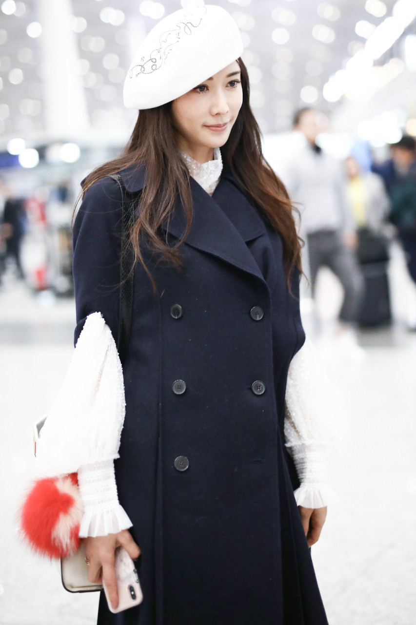 林志玲戴白色贝雷帽穿黑色长款大衣现身机场,皮肤白皙面带微笑