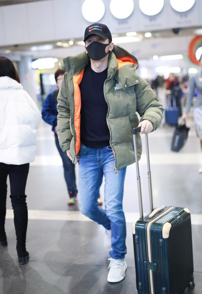 身穿厚实羽绒服的他单手推箱子并拿着机票钱包等