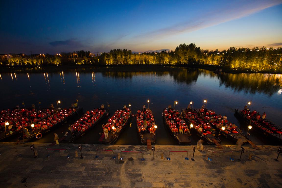 停泊在溪边的船只燃起了暖黄色的船灯,一排船灯映照着粉色的桃花,和