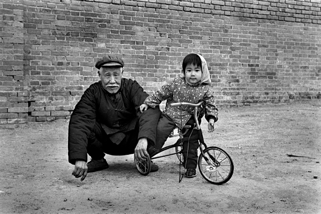 七十年代一个大爷带着孙女在胡同里玩耍,小女孩骑着儿童三轮车