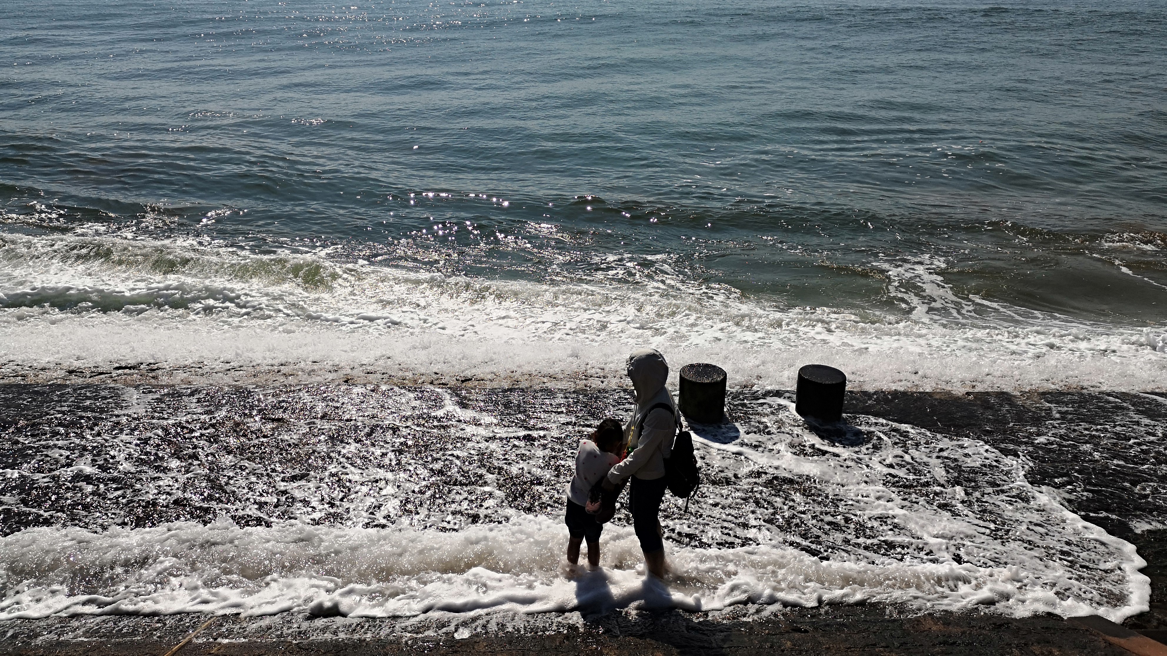 青岛的海波光粼粼,母女海边嬉戏踏浪而行,迎接扑面而来的波涛!