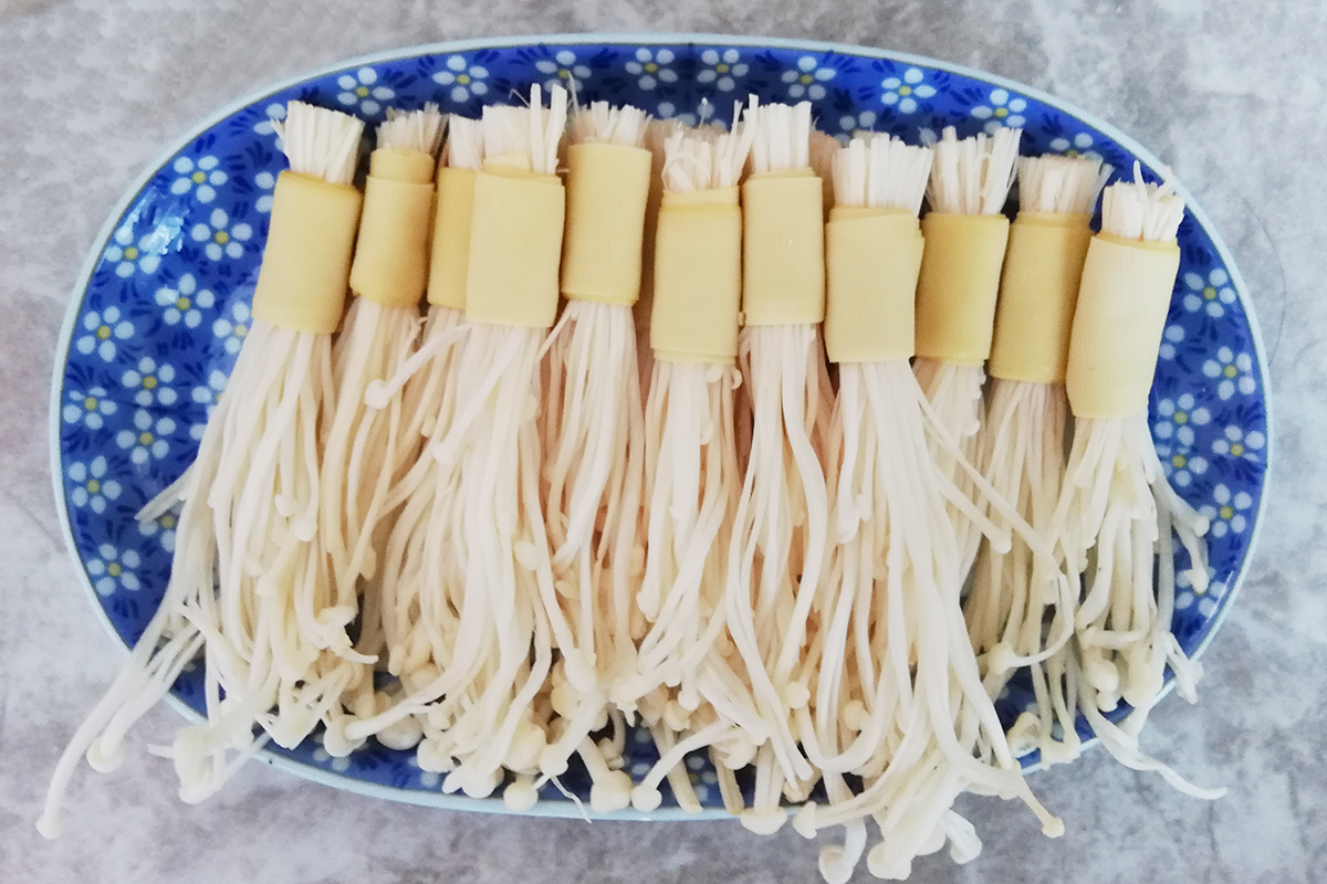 取1根火腿肠粗的金针菇,然后用1小条豆皮将其卷起来,用牙签固定住