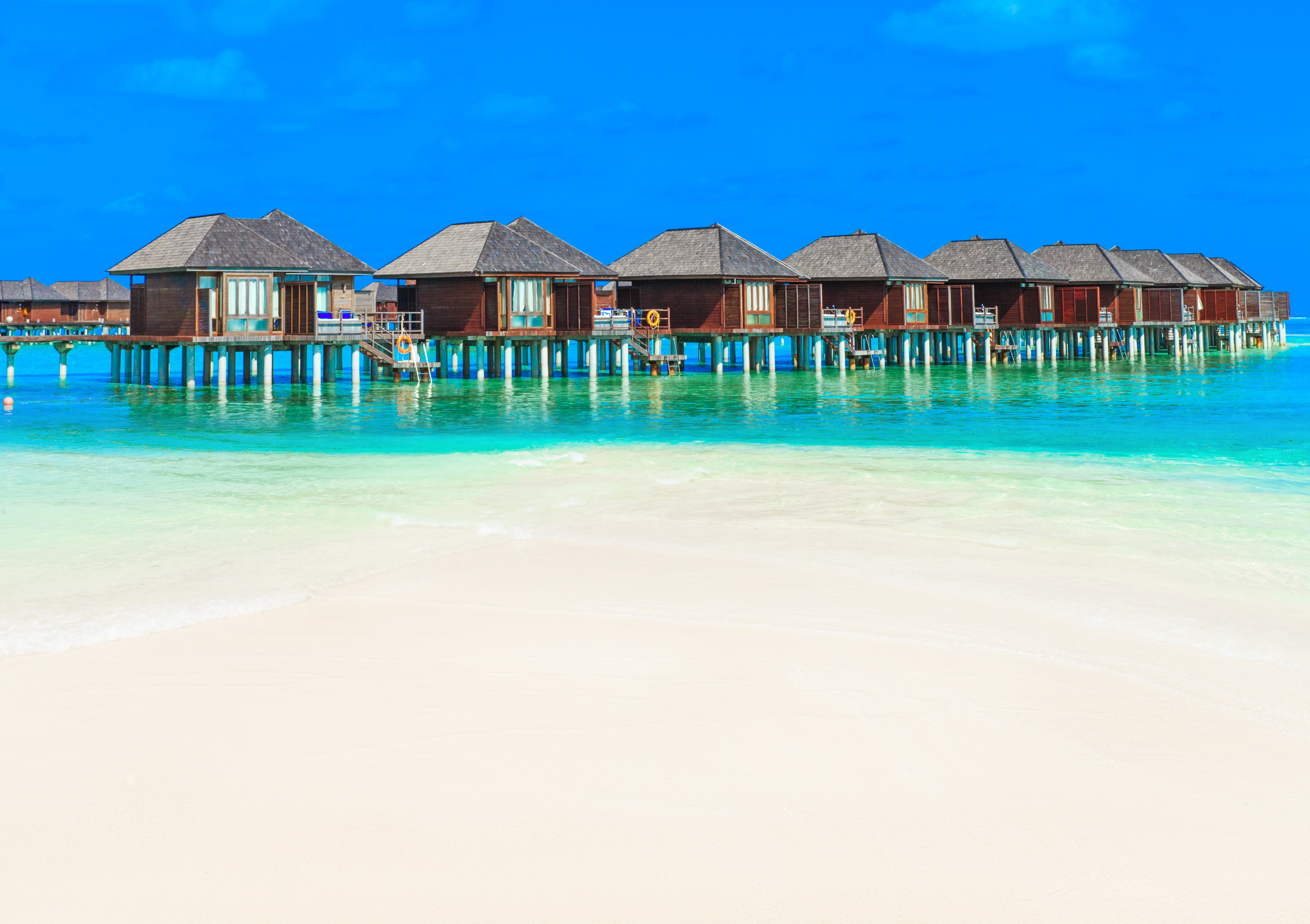 蓝白相间的海景:屹立在海上的房屋,米白色的沙滩,淡蓝色的海水平静的