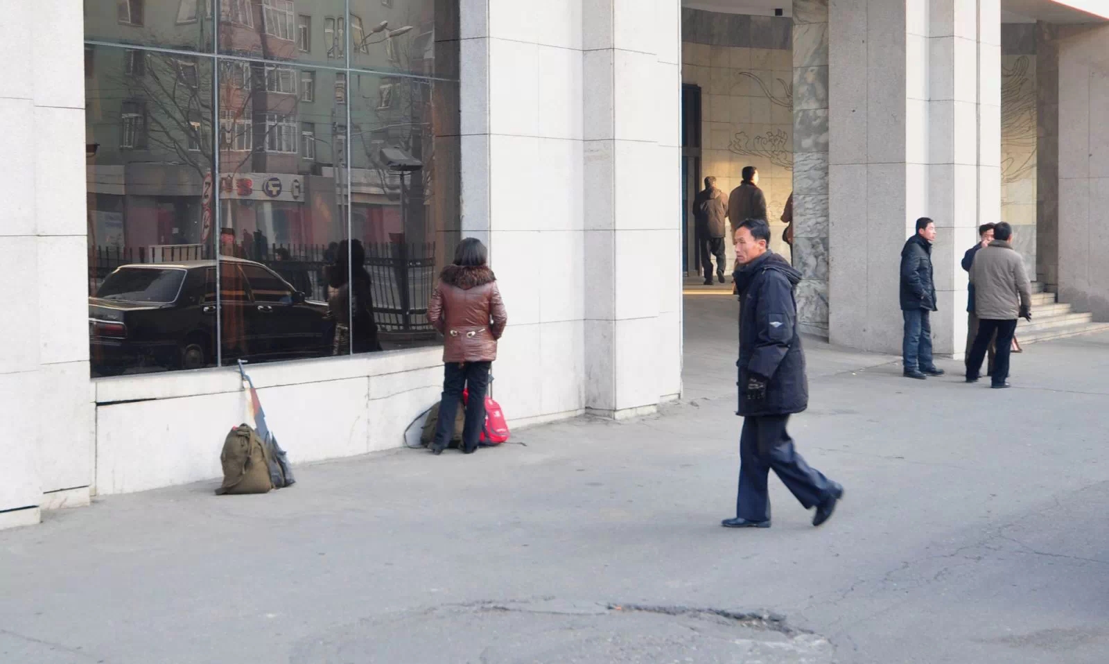 图为朝鲜平壤街头,一名朝鲜女子在墙角休息,墙角放着包裹和一把枪.