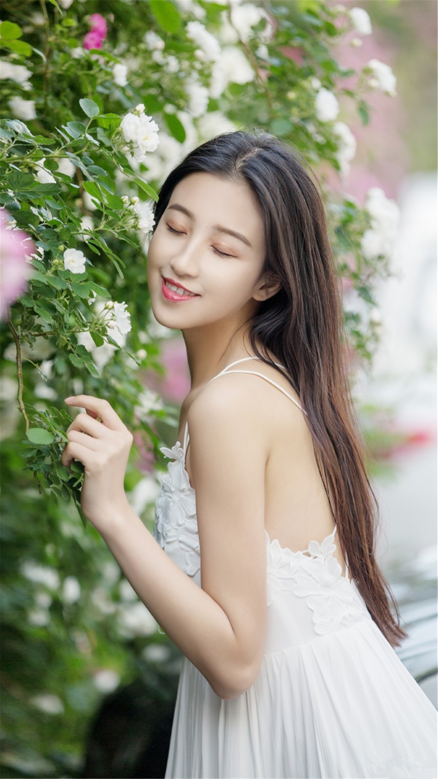 一位穿白色吊带裙的女孩,她秀发披肩,微笑迷人