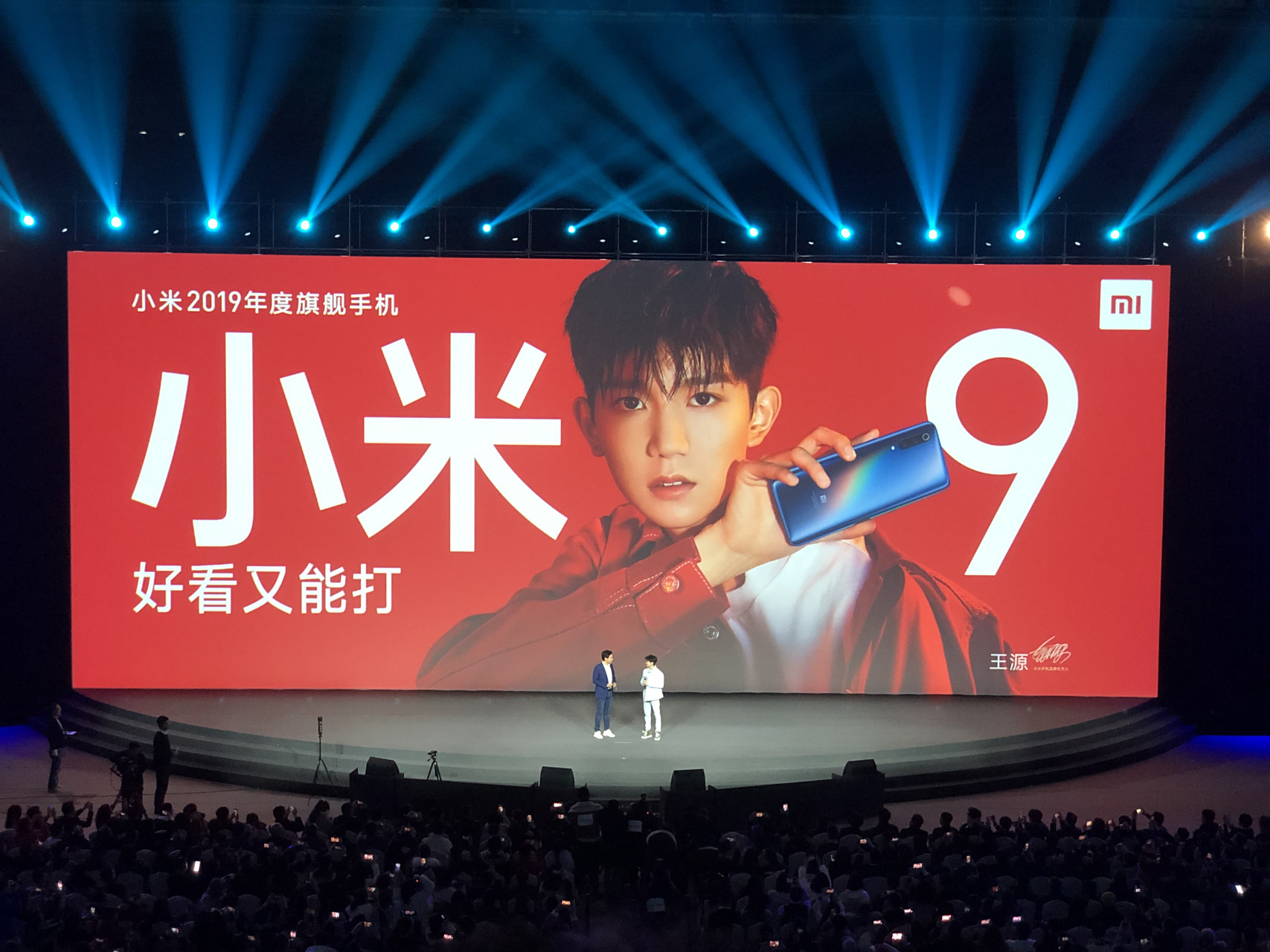 雷军邀请小米9代言人王源一同上台展示,全息幻彩色的小米9和青春帅气