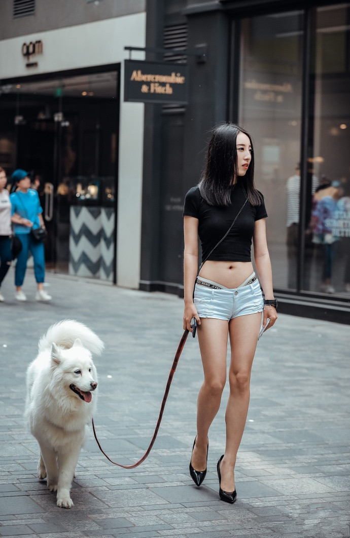 这位牵着狗狗的美女,有着乌黑的长发,搭配黑色紧身上衣和超短裤,美丽