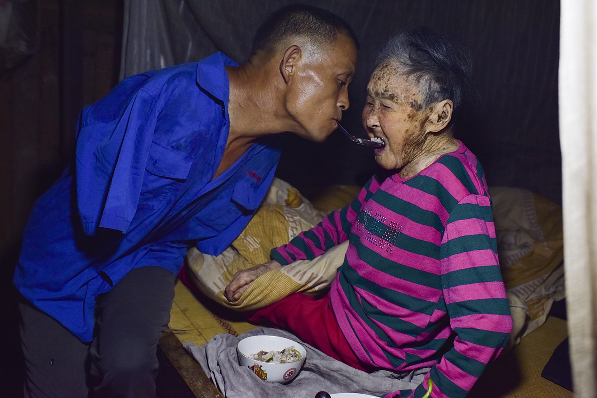 图片中这位被称作"无臂孝子"的重庆男子陈星银,正在用嘴衔着饭勺给年