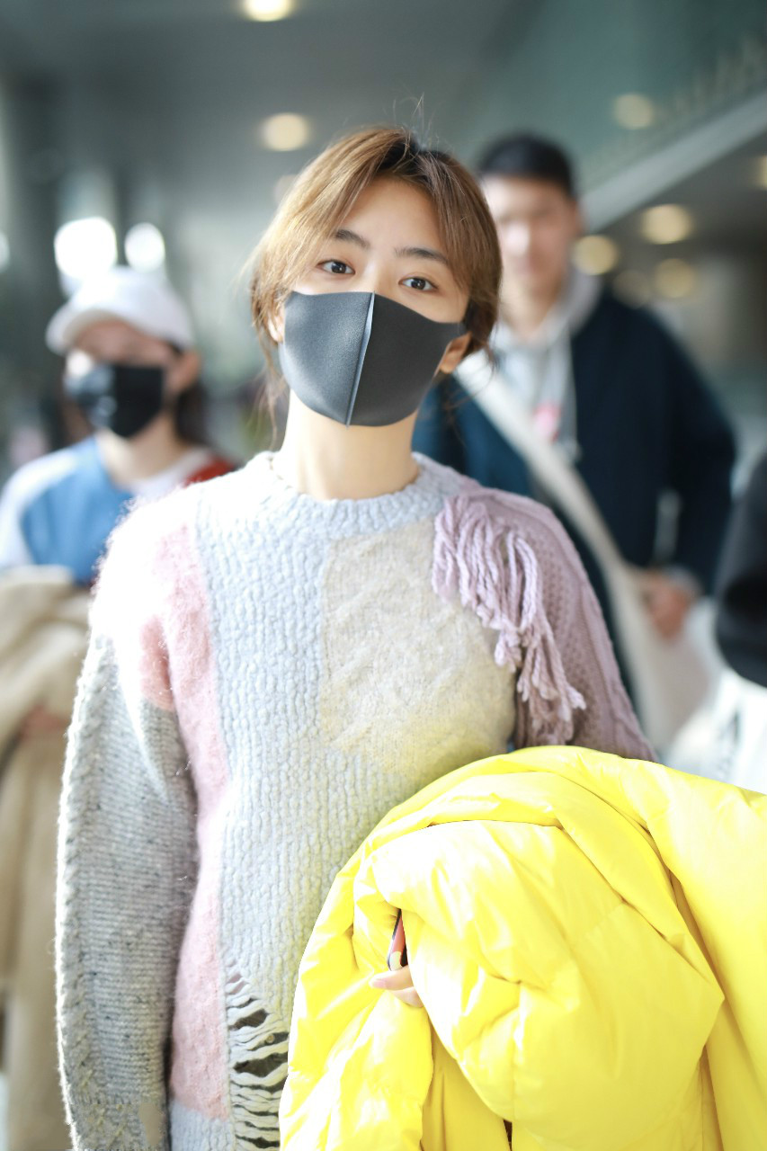 谭松韵戴口罩穿毛衣搭配牛仔裤现身机场,手里拿着黄色羽绒服
