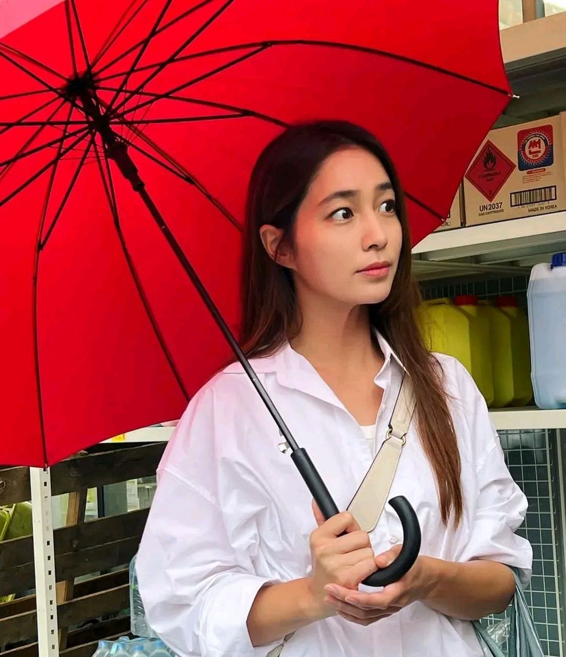 公开的照片中,李敏贞身穿白色衬衫,手里拿着红色雨伞望着某处.