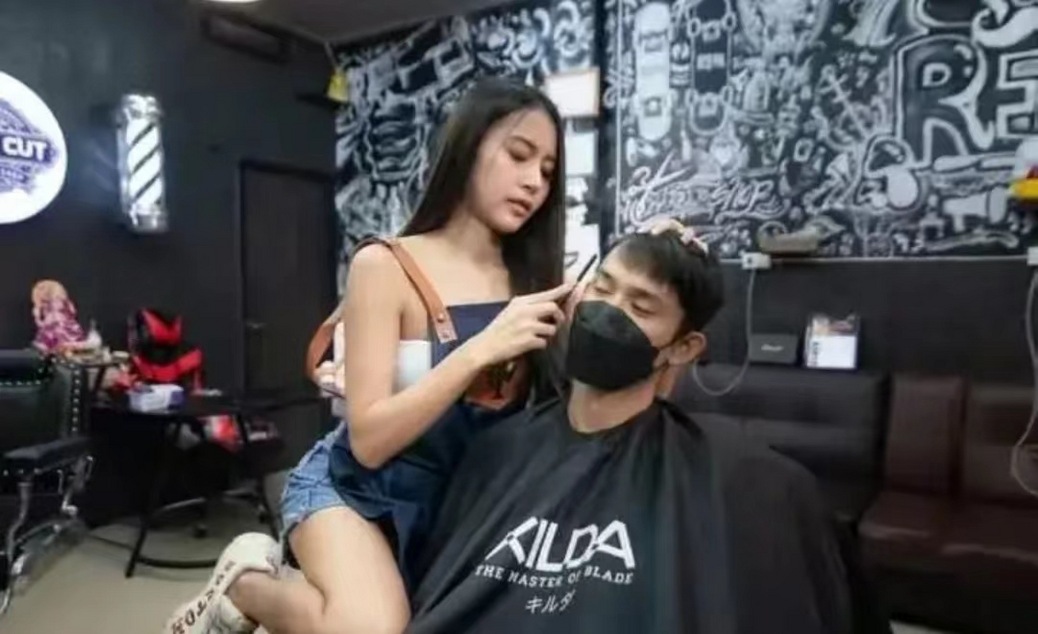 泰国某家理发店,两名美女理发师正在为一名男顾客剪头时的场景