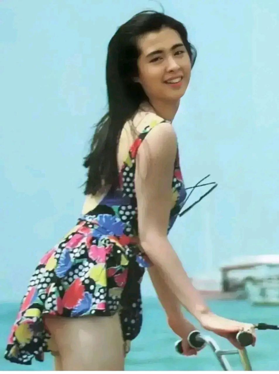 图为王祖贤年轻漂亮,一袭花色泳衣更显青春活力,胸悬墨镜,侧身面对