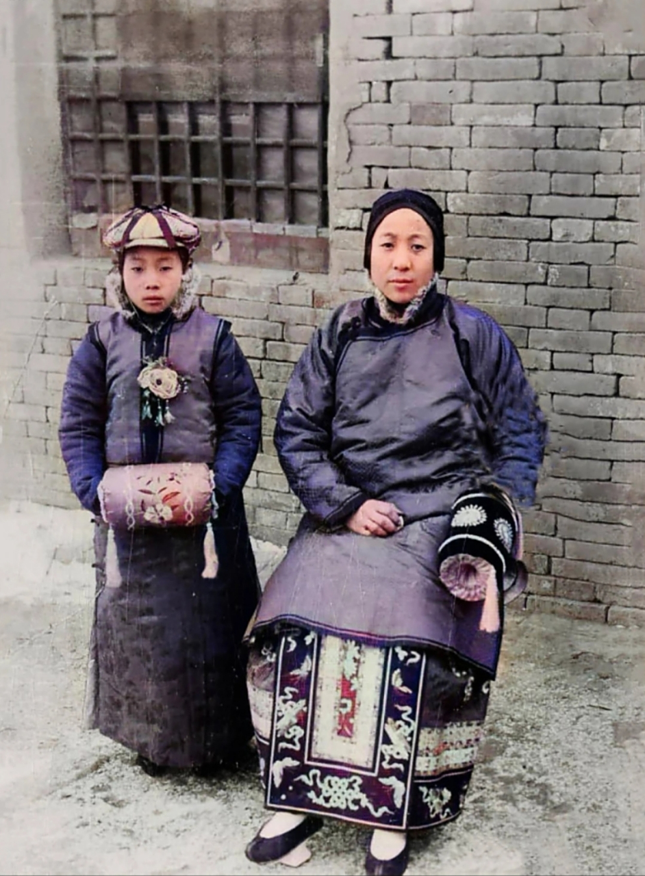 母亲头戴抹额,下着袄裙,脚踩"高底鞋",旁边的男子,穿着缎子长袍,批着