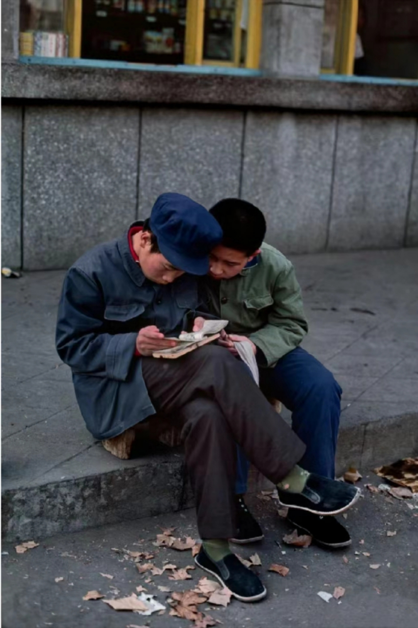1984年,北京街头,两个少年坐在街头正在看小人书,这是秋日时分,梧桐叶