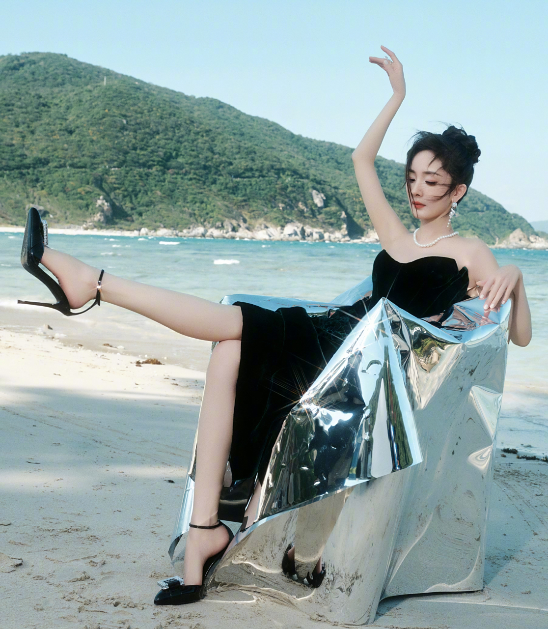 杨幂海滩上拍摄,穿着黑色连衣裙,坐在一个闪亮的椅子上,背景是大海和