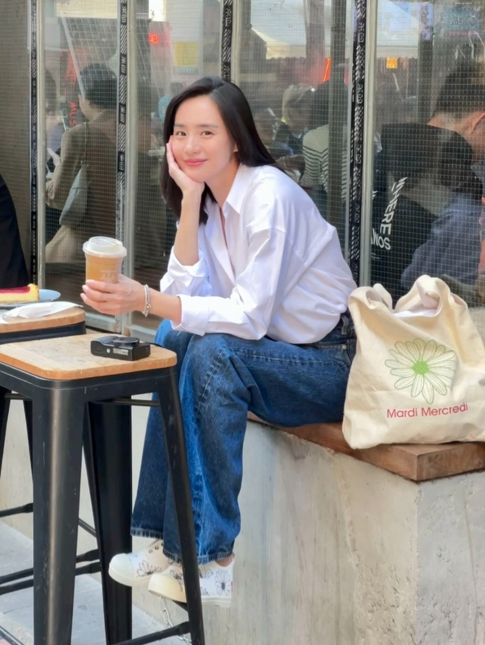 王智的休闲风格美照,穿着宽松的白衬衫和牛仔裤,端着泥巴色奶茶杯