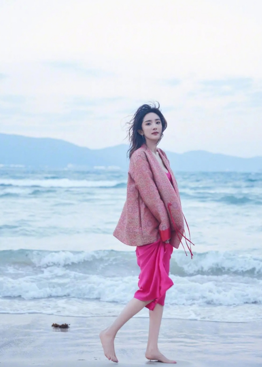 杨幂穿粉丝吊带裙行走在海边,身材优美,微卷发型轻盈飘逸,宛如海中的