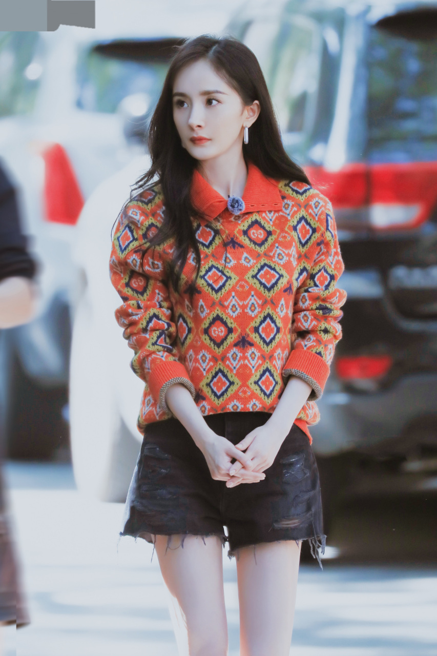 杨幂街拍图,一头黑色披肩长发,身着红色长袖衫搭配黑色短裤,脚踩白色