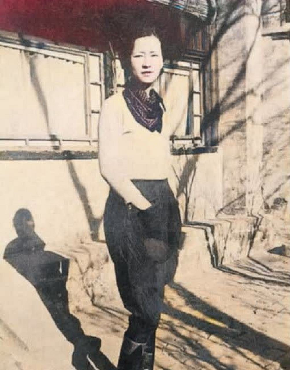 照片中,林徽因身穿白色上衣,脖子上围着丝巾,下穿一条黑色长裤,脚踩