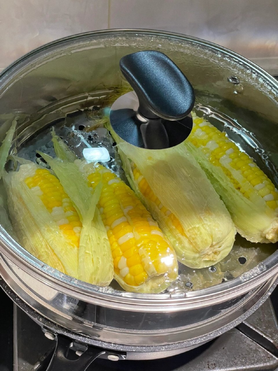 当水咕噜咕噜沸腾起来后,放上蒸架,把玉米留点皮,隔水蒸起来.