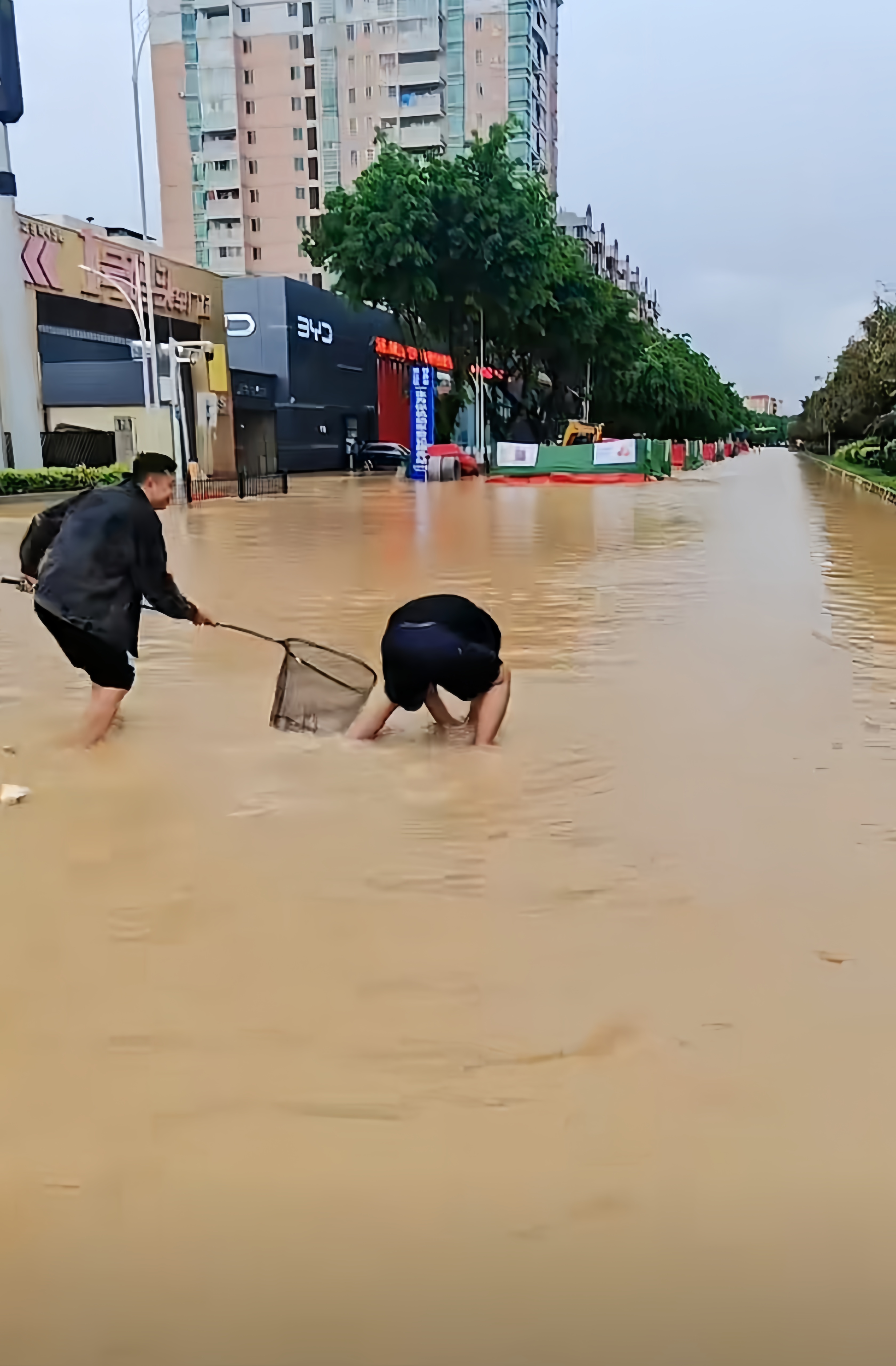 洪水爆发过后,水淹没了好多街道,这俩人的心态真好,还在抓鱼