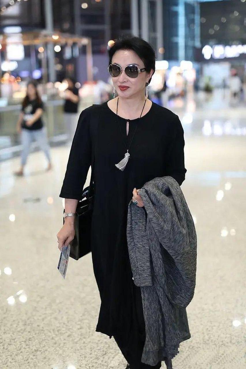53岁金星走机场,黑裙配运动鞋超低调,盘起头发大气又优雅!
