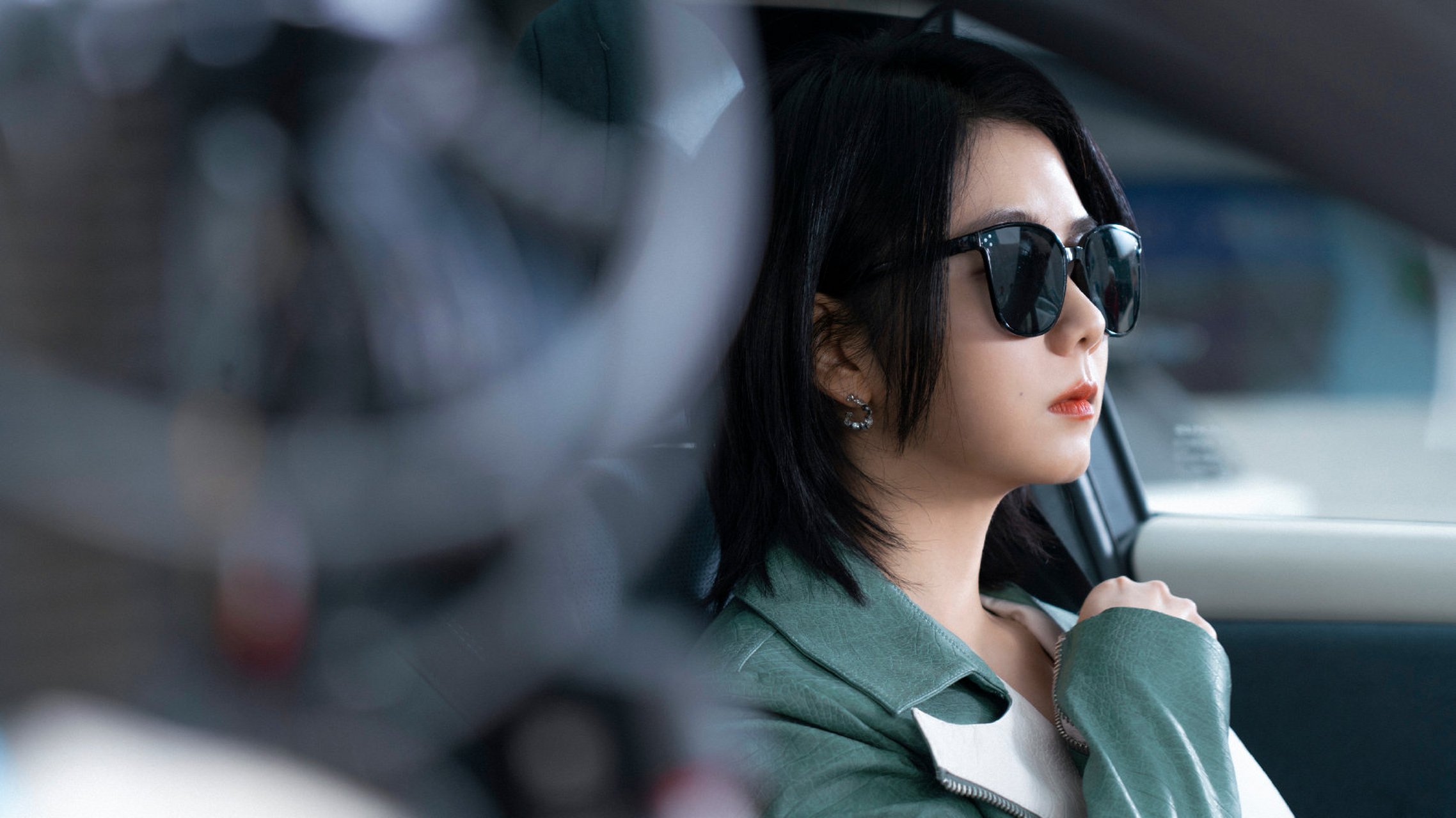 谭松韵身穿青绿色外套,短发造型搭配黑色墨镜,坐在车里的样子,非常有