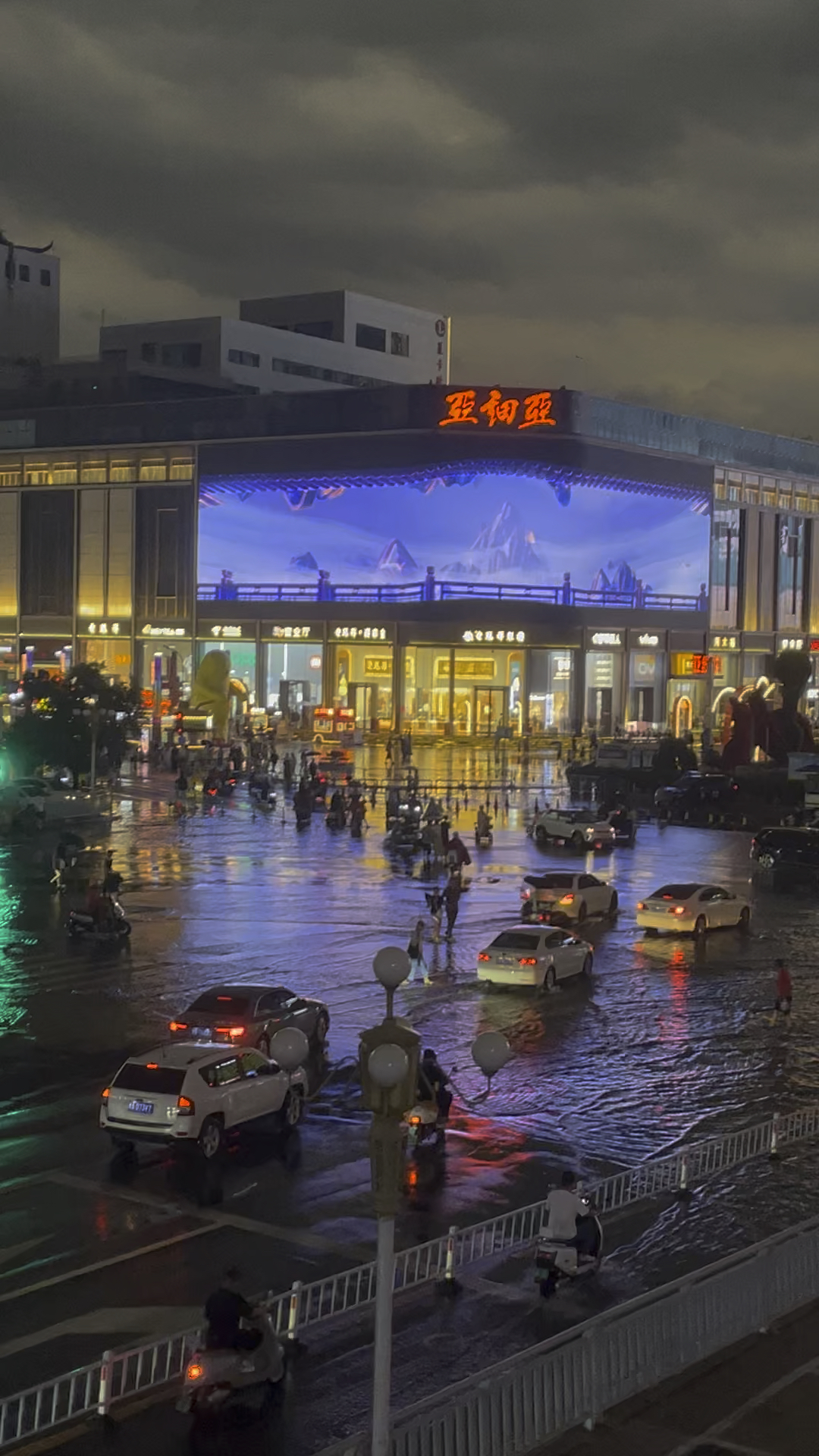 郑州亚细亚门口,暴雨积水严重,汽车行人缓慢,二七塔风雨中矗立