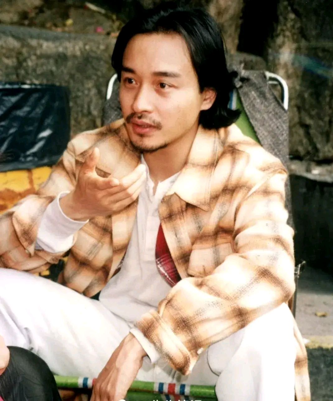 照片里张国荣坐在一把简陋的椅子上,留着长头发,满脸胡子,艺术气息